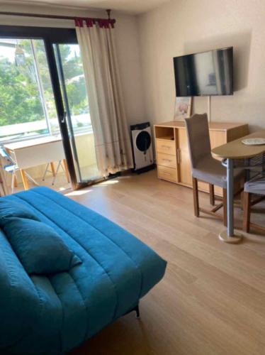 Cette chambre comprend un lit bleu, un bureau et une télévision. dans l'établissement LES GABIANS - Appartement T2 - TIKI PLAGE - Saint Raphaël, à Saint-Raphaël
