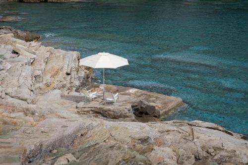 an umbrella and two chairs sitting on the rocks near the water at Kea Blue Heaven in Koundouros