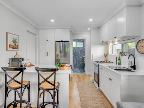 Una cocina con gabinetes blancos y dos taburetes de bar. en Comfort Cove - quiet luxury with full kitchen, en Brisbane