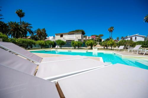 a swimming pool with white umbrellas and palm trees at Villa Venera Fontane Bianche Charme Apartments in Fontane Bianche