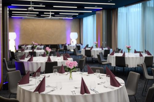 a conference room with white tables and chairs and pink flowers at Mercure Debrecen in Debrecen
