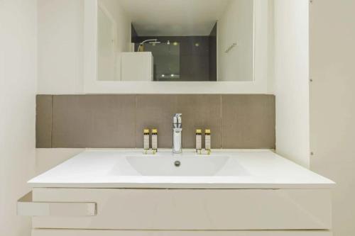 une salle de bain blanche avec un lavabo et un miroir dans l'établissement Sublime Appartement Parisiens, à Paris