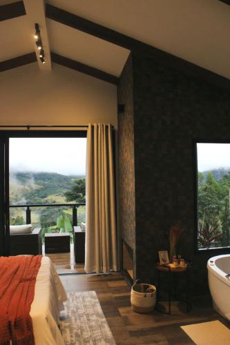 a bedroom with a bed and a tub and a large window at Chalés Vale da Mantiqueira- chalé 2 in Bueno Brandão