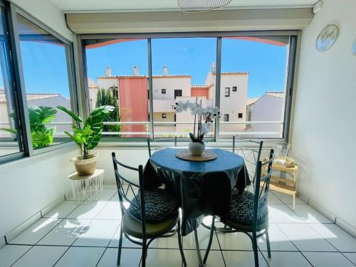 une table et des chaises dans une pièce avec des fenêtres dans l'établissement Cap Studio Parking Wifi Port Plage, au Cap d'Agde