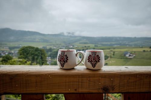 two coffee mugs sitting on top of a wooden rail at HRYCÓWKA Domki z Widokiem in Grywałd