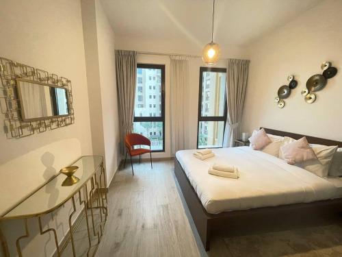 a bedroom with a bed and a desk and two windows at Luxe & Comfy Madinat Jumeirah - Apartment with Scenic Views - Pool Managed by SunnyHomes in Dubai
