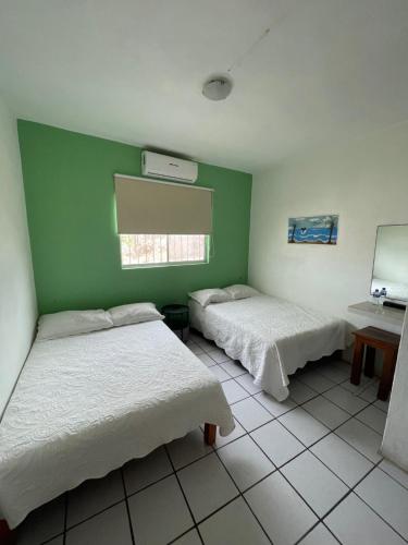 two beds in a room with a green wall at Hotel Oasis Cuyutlan in Cuyutlán