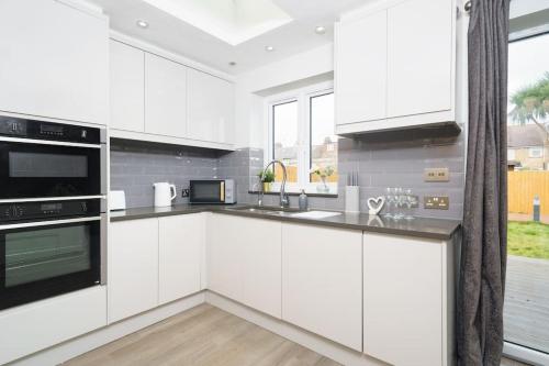 a kitchen with white cabinets and a large window at Beautiful 4 Bed Immaculate Condition Refurbished Property in Romford