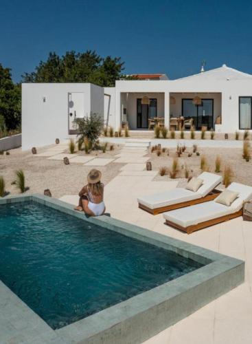 a woman sitting next to a swimming pool next to a house at Casa Bartolomeu in Castro Marim