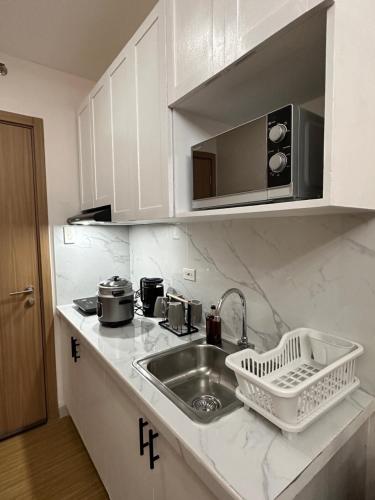 a white kitchen with a sink and a microwave at Cozy Condo in Taguig in Manila