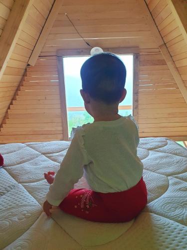 a young child sitting on a bed looking out a window at Mountain View in Foča