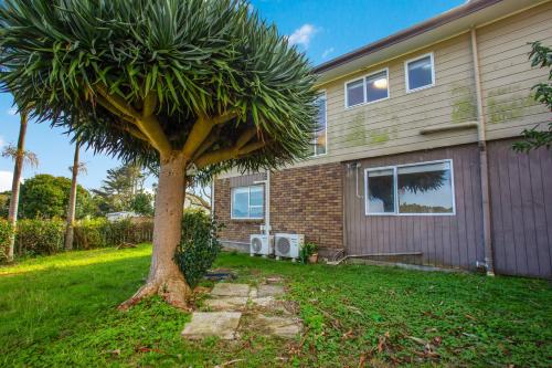 a palm tree in front of a house at Sandy Feet Retreat close to Beach in Clarks Beach