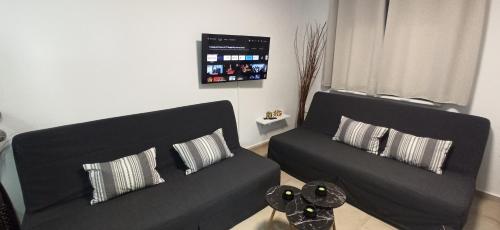 a living room with two black couches and a tv at AXD Evangelia's apartment in Alexandroupoli