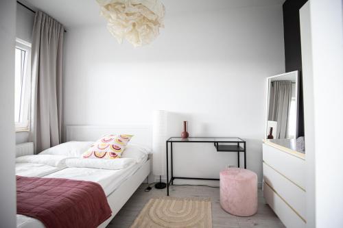 a white bedroom with a bed and a pink stool at Seaside Apartment in Gdańsk