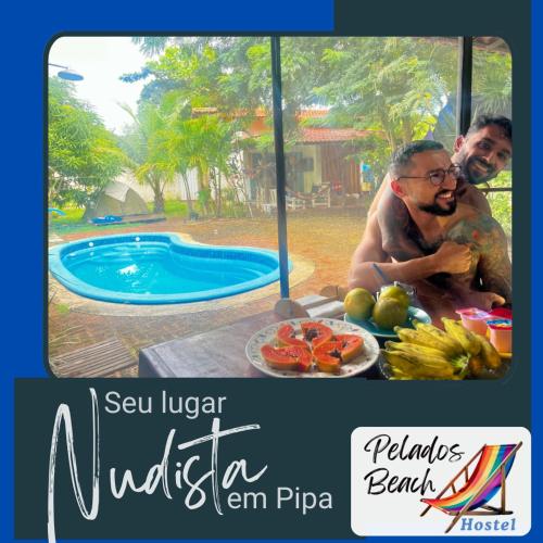 two men sitting at a table next to a swimming pool at Pelados Beach Hostel in Pipa