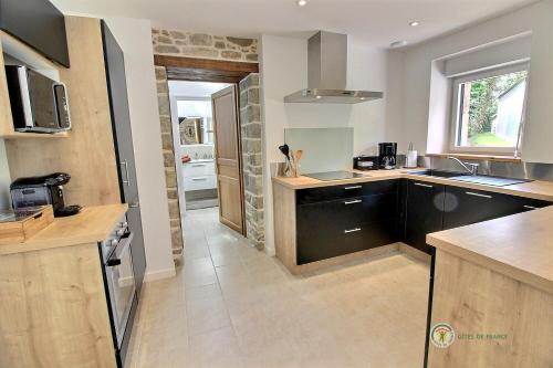 une cuisine avec des placards noirs et un mur en pierre dans l'établissement Crech ar feuteun, à Lanvellec