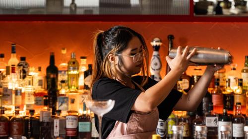 a woman standing behind a bar holding a bottle of alcohol at Hotel Indigo Sydney Potts Point by IHG in Sydney