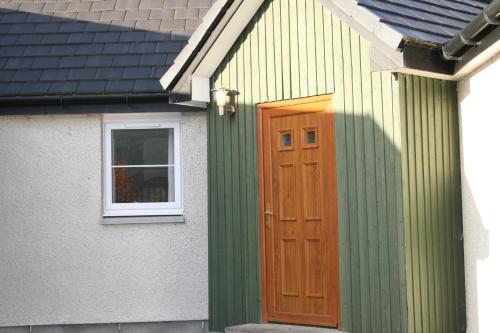 a green house with a wooden door and a window at BCC Loch Ness Hostel in Bearnock