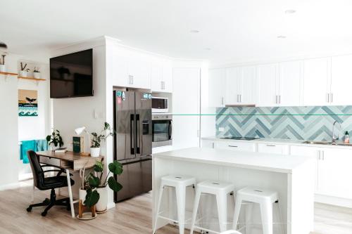 a kitchen with white cabinets and a table with stools at Driftwood Callala Plus - Jervis Bay Getaway - 10 Guests! in Callala Bay