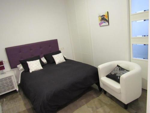 a bedroom with a bed and a white chair at Apartamentos Ilíberis in Granada
