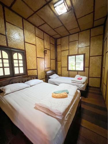 two beds in a room with wooden walls and windows at ไชยพล โฮมสเตย์ หมู่บ้านแม่กำปอง in Ban Pok Nai