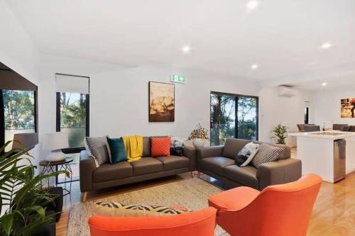 a living room with two couches and a kitchen at Treetops-Large Home 9km to CBD Sleeps 10 in Hobart