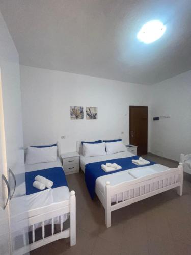 two beds in a white room with blue sheets at Vogue Rooms in Golem