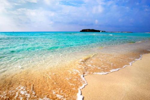 a beach with water and an island in the background at Tala Hills Sea View Apartment, Tala Village, Paphos in Tala