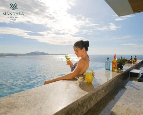 a woman sitting at a table by the water with a drink at APEC Mandala Mũi Né in Mui Ne