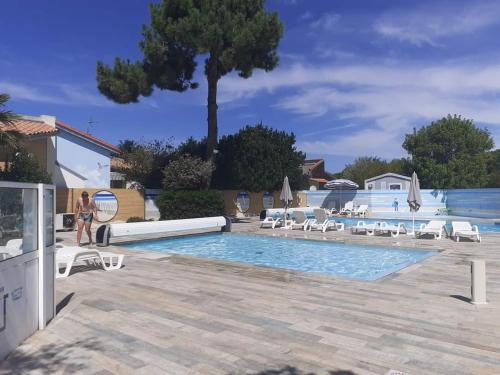 une femme debout à côté d'une piscine avec des chaises dans l'établissement Mobil-Home 4-6 personnes dans camping 3 étoiles, à Saint-Pierre-dʼOléron
