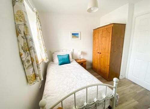 a bedroom with a white bed and a wooden cabinet at Moore Bay Holiday Homes No 18A by Trident Holiday Homes in Kilkee