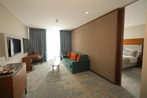 sala de estar con sofá verde y cama en Dedeman Cizre Hotel, en Jesıret ibn Omar