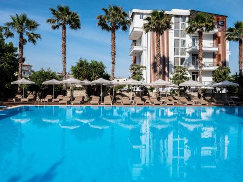 a large swimming pool with chairs and palm trees at Nia Boutique Hotel by Rapo's Resort in Himare