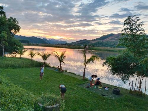 a group of people sitting on the grass by a river at Village House in Phong Nha