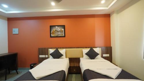two beds in a room with an orange wall at Hotel Hive Inn - Kozhikode in Kozhikode