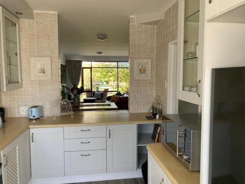a kitchen with white cabinets and a living room at Your own space in the leafy Cape in Cape Town
