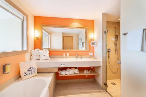 a bathroom with a tub and a sink and a mirror at Strandhotel Seerose in Kolpinsee