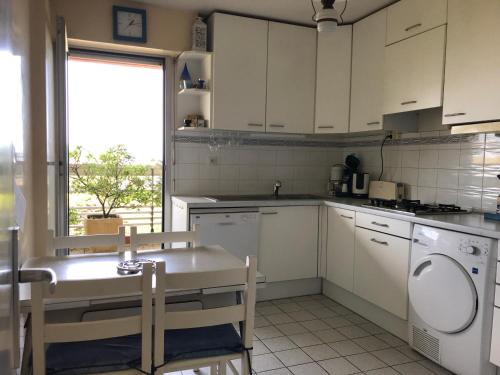 une cuisine avec des armoires blanches, une table et une fenêtre dans l'établissement Hippocampe, à Anglet