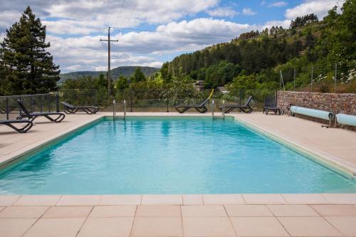 a swimming pool with blue water and benches around it at Village de gîtes de Barre-des-Cévennes in Barre-des-Cévennes