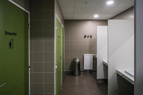 een badkamer met groene en witte tegels en een prullenbak bij Auberge de jeunesse HI Clermont-Ferrand in Clermont-Ferrand