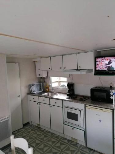 Il comprend une cuisine avec des placards blancs et une télévision. dans l'établissement Bungalow cosy à Commequiers avec piscine partagée, à Commequiers