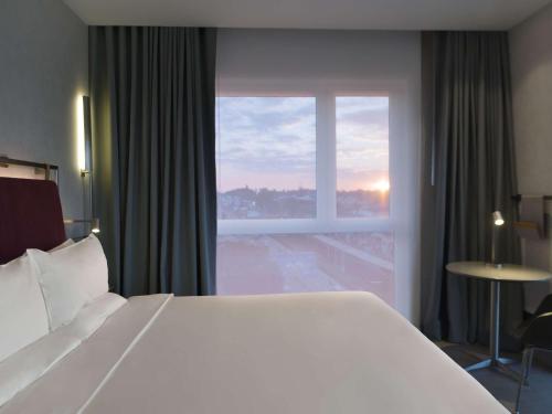 a large white bed in a hotel room with a window at Novotel Lubumbashi in Lubumbashi