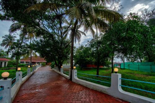 a walkway with a fence and palm trees in a park at Papilio Beach Front Cottages-TBV in Baga