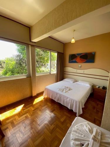 a hotel room with two beds and two windows at Hotel Cataguases in Cataguases