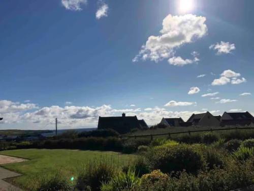 a house in a field with the sun in the sky at Seaside Chic! Modern Cosy Home in Lahinch