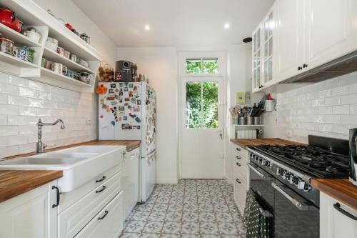 La cuisine blanche est équipée d'un évier et d'un réfrigérateur. dans l'établissement Charmante Maison au Raincy, à Le Raincy