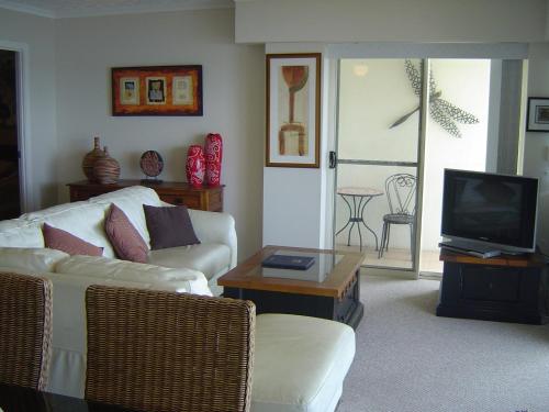 a living room with a white couch and a tv at Moorings Beach Resort in Caloundra