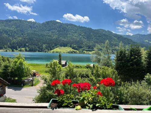 a view of a lake with red flowers and mountains at Pferdehof Rupitsch - Haus Carina in Weissensee
