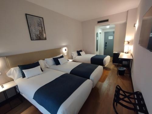 a hotel room with two beds and a desk at Hotel Don Jaime 54 in Zaragoza
