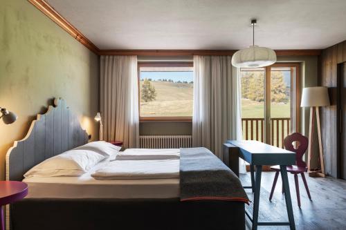 a bedroom with a bed and a desk and a window at ICARO Hotel in Alpe di Siusi